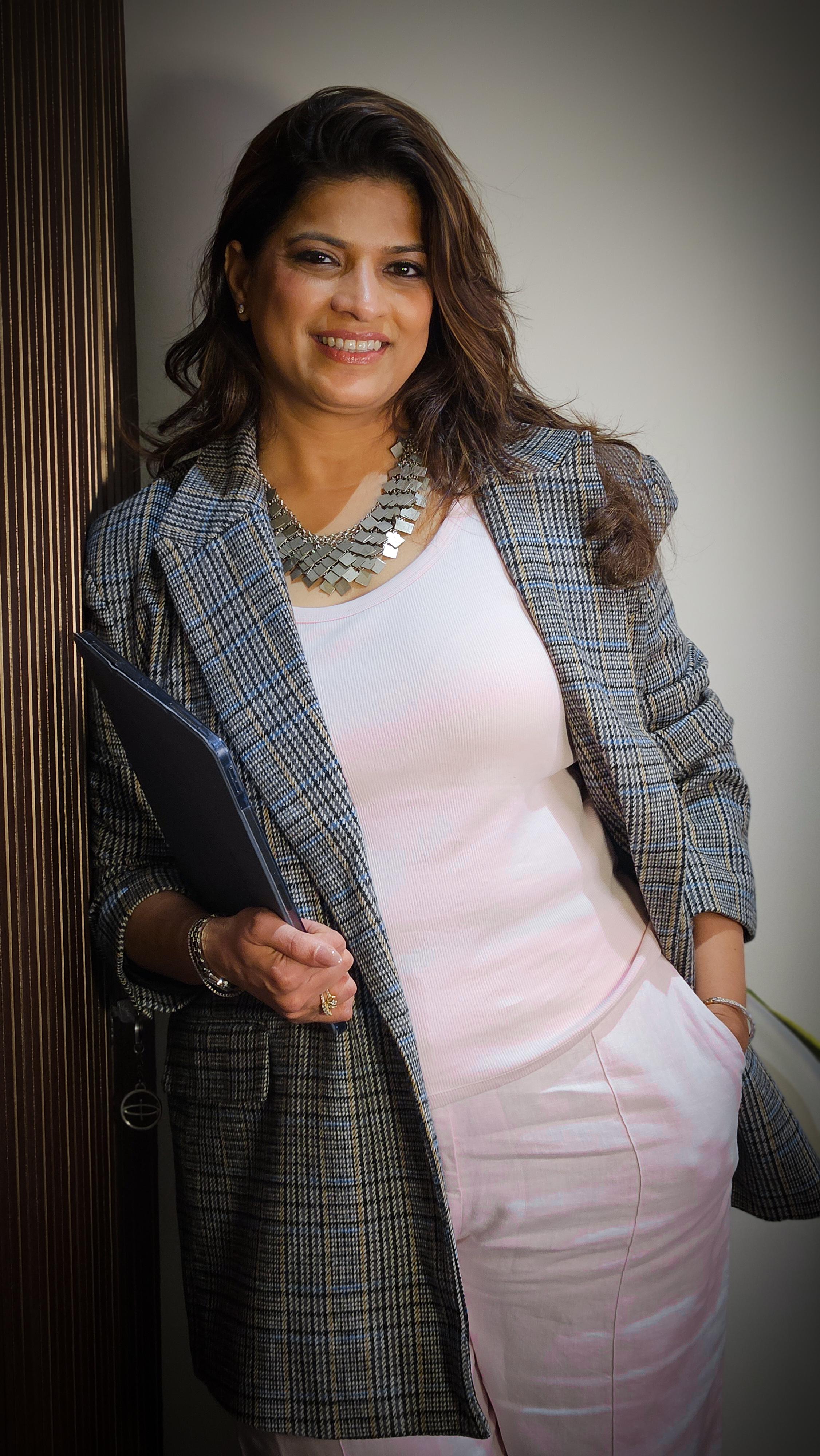 Abhilasha Lonari smiling in a checked blazer and holding a black folder