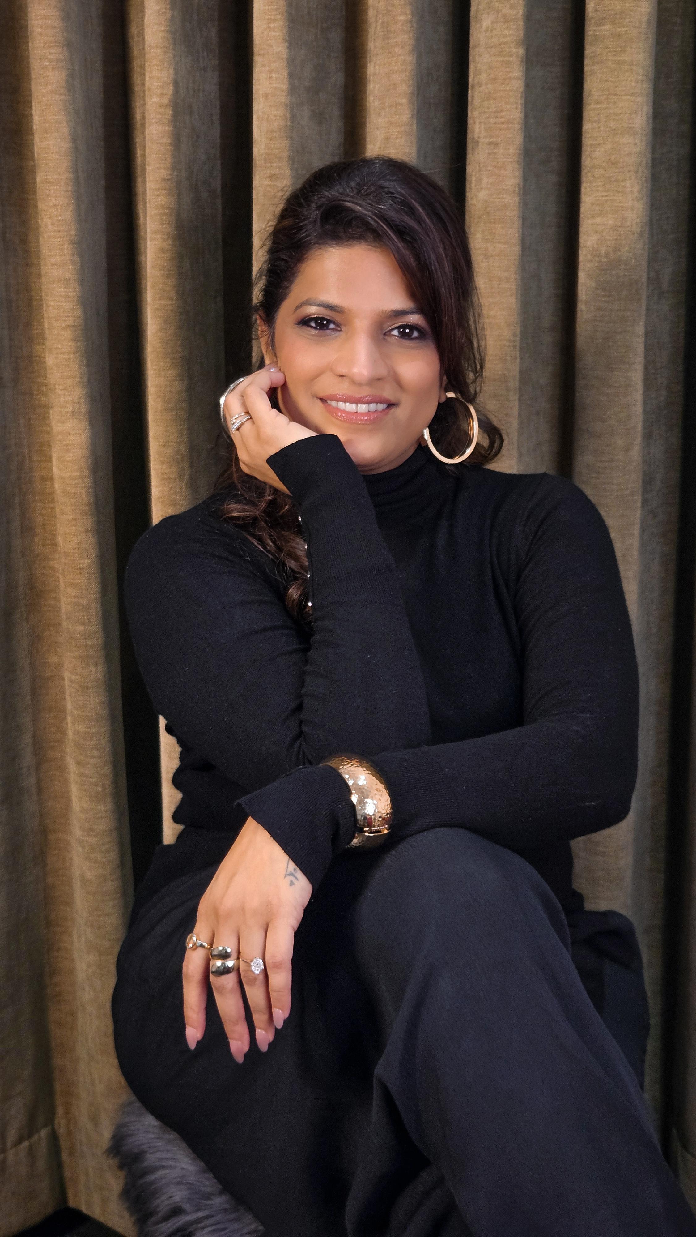 Portrait of Abhilasha Lonari seated in black against warm brown curtains