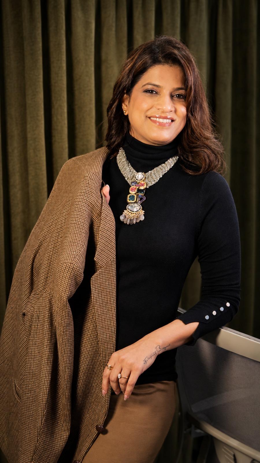 Abhilasha Lonari smiling in a black turtleneck with a brown jacket draped over her shoulder